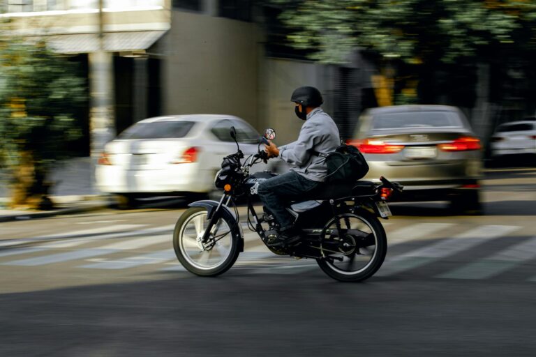 A motorcyclist wearing a helmet rides through city traffic on a bright day.